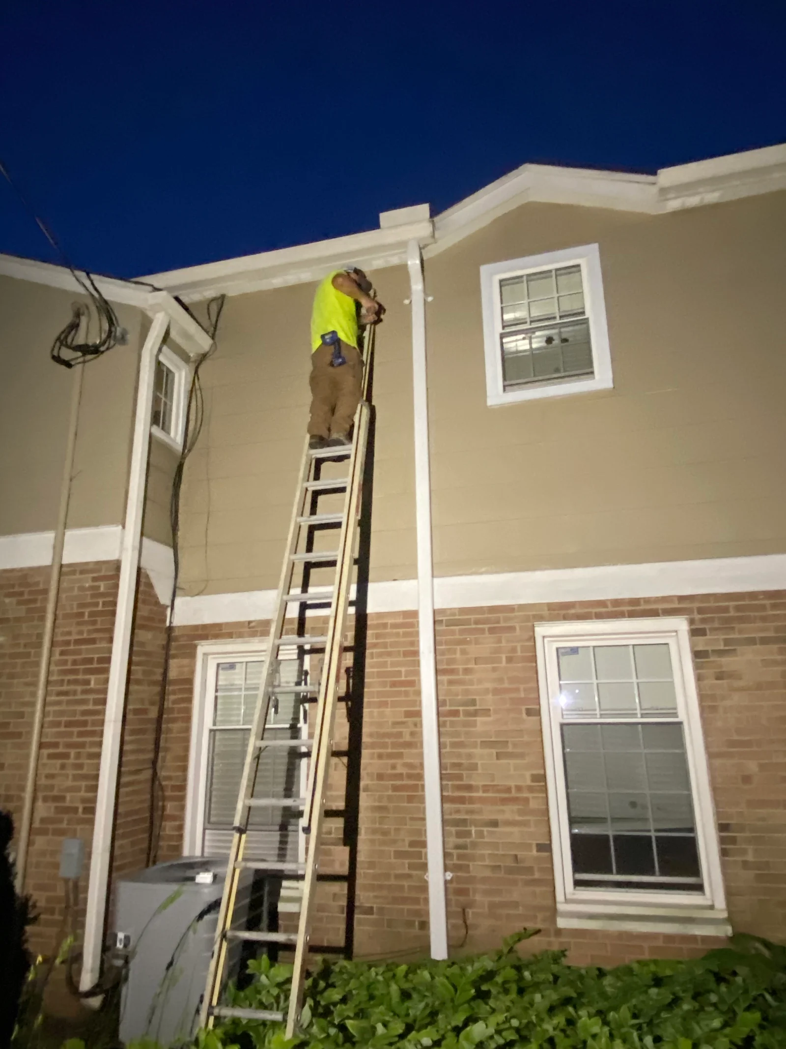 A worker on a ladder beside exterior siding and upper-level trim